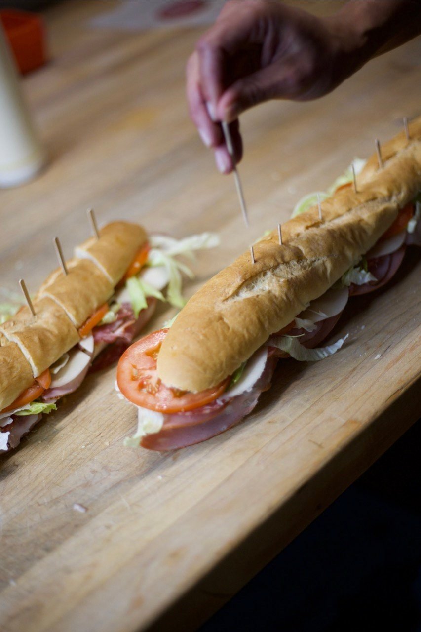 A long baguette sub being built by hand